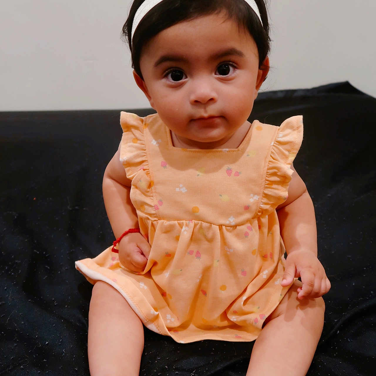 Arliss Selah is registered to the contest to win money with this photo: baby, barefoot, black_background, child, curious, cute, dress, fashion, feet, flower, hands, headband, indoors, infant, peach_color, person, portrait, sitting, skin, young_child