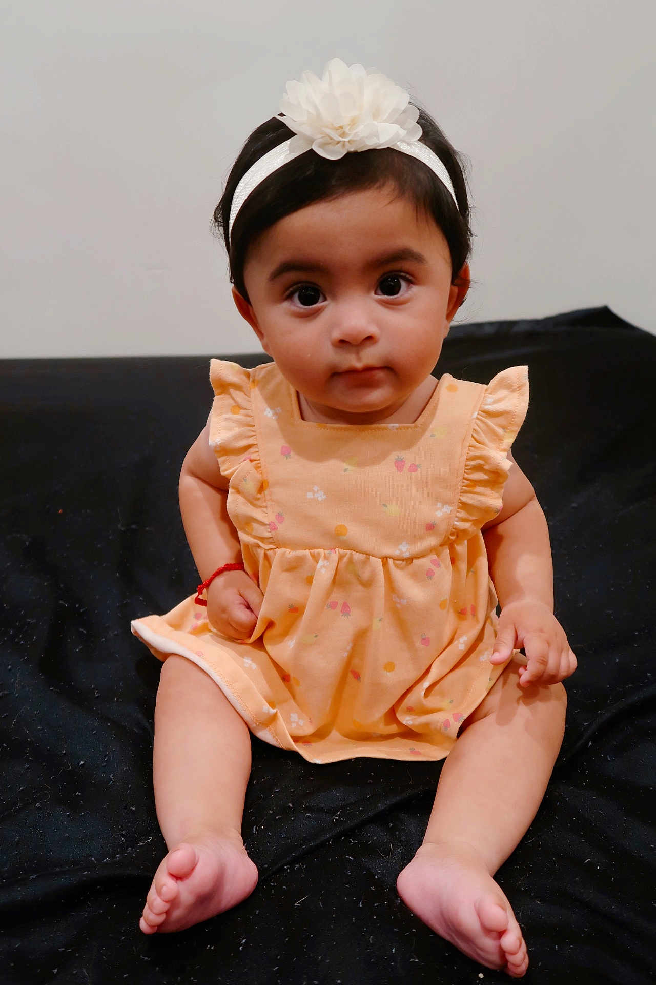 Arliss Selah is registered to the contest to win money with this photo: baby, infant, child, headband, flower, dress, peach_color, sitting, barefoot, cute, curious, indoors, portrait, person, young_child, black_background, skin, hands, feet, fashion
