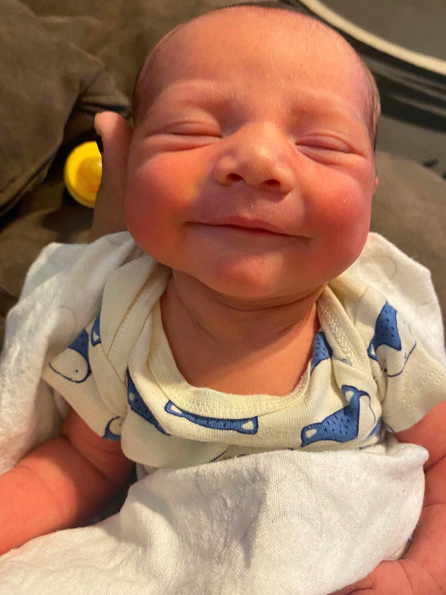 Easteynn is registered to the contest to win money with this photo: baby, newborn, smiling, face, blanket, onesie, blue_pattern, white_clothing, infant, resting, couch, soft_texture, skin, hand, comfort, closeup, child, indoors, peaceful, sleepy