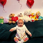 Matilda joined the competition — help win amazing prizes! baby, child, stuffed_animals, toys, balloons, heart_shaped, couch, smiling, sitting, colorful, decor, indoor, happy, cute, plush, clothing, person, face, celebration, home