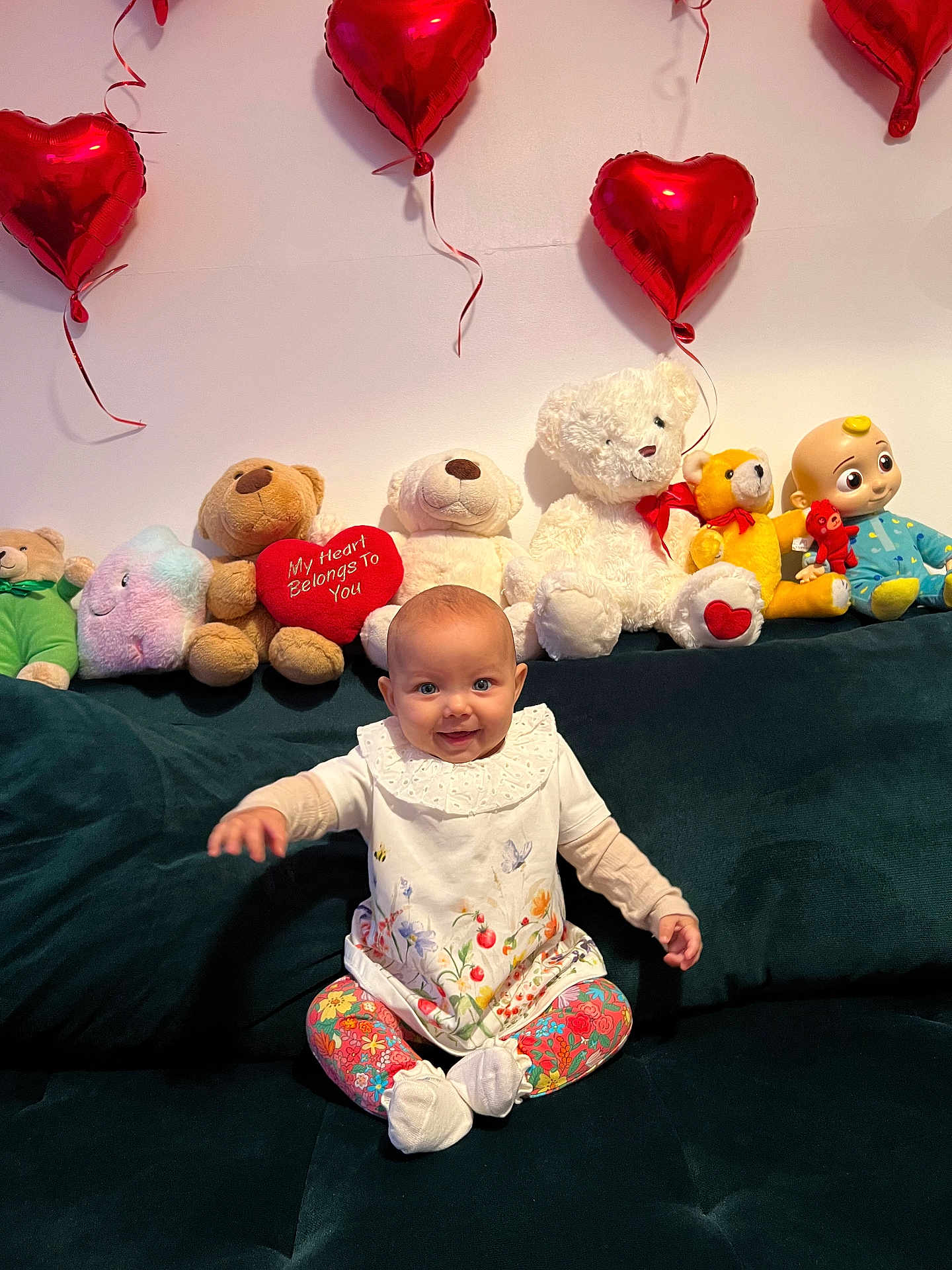 Matilda joined the competition — help win amazing prizes! baby, child, stuffed_animals, toys, balloons, heart_shaped, couch, smiling, sitting, colorful, decor, indoor, happy, cute, plush, clothing, person, face, celebration, home