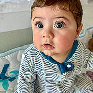 Damian joined the competition — help win amazing prizes! baby, child, infant, onesie, striped_clothing, face, eyes, cheeks, mouth, skin, hair, hand, baby_bed, blanket, blue, white, indoor, portrait, cute, curious