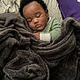 baby, sleeping, blanket, green_clothing, bed, face, curly_hair, infant, cozy, child, pajamas, soft_texture, resting, indoors, peaceful, toddler, cushion, sleep, comfort, portrait