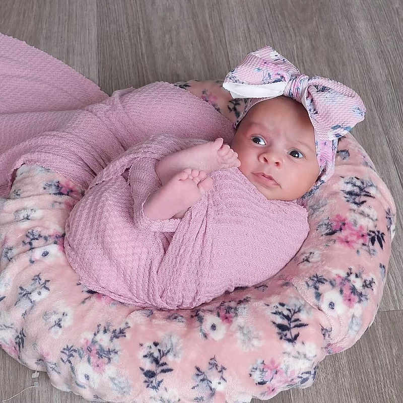 Lila is registered to the contest to win money with this photo: baby, blanket, bow, child, cozy, cushion, cute, floor, floral, headband, indoors, infant, lying_down, newborn, person, pink, portrait, soft_texture, wooden_floor, wrapped