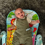 Jamie joined the competition — help win amazing prizes! animal_print, baby, baby_toy, carpet, child, clothing, colorful, cute, face, floor, happy, indoor, infant, person, play_mat, sitting, smiling, striped_overalls, toy, young_child