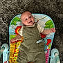 animal_print, baby, baby_toy, carpet, child, clothing, colorful, cute, face, floor, happy, indoor, infant, person, play_mat, sitting, smiling, striped_overalls, toy, young_child