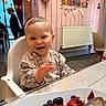 baby, high_chair, smiling, waving, indoor, cafe, pancakes, fruit, strawberries, blueberries, plate, spoon, table, decorations, bunting, lights, pink_wall, person, child, happy