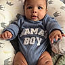 baby, infant, child, blue_clothing, mamas_boy_text, cushion, blanket, bed, indoor, cute, smiling, portrait, hands, legs, face, eyes, cozy, soft_texture, patterned, comfortable