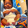 baby, infant, smiling, blanket, car_seat, dinosaur_pattern, paw_prints, clothing, feet, hands, face, cute, cozy, indoors, child, portrait, happy, wrapped, colorful, soft