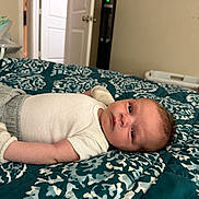 Greyson is registered to the contest to win money with this photo: baby, infant, bed, blanket, pattern, clothing, white_shirt, grey_pants, socks, indoor, room, door, furniture, lying_down, face, person, calm, soft_lighting, home, portrait