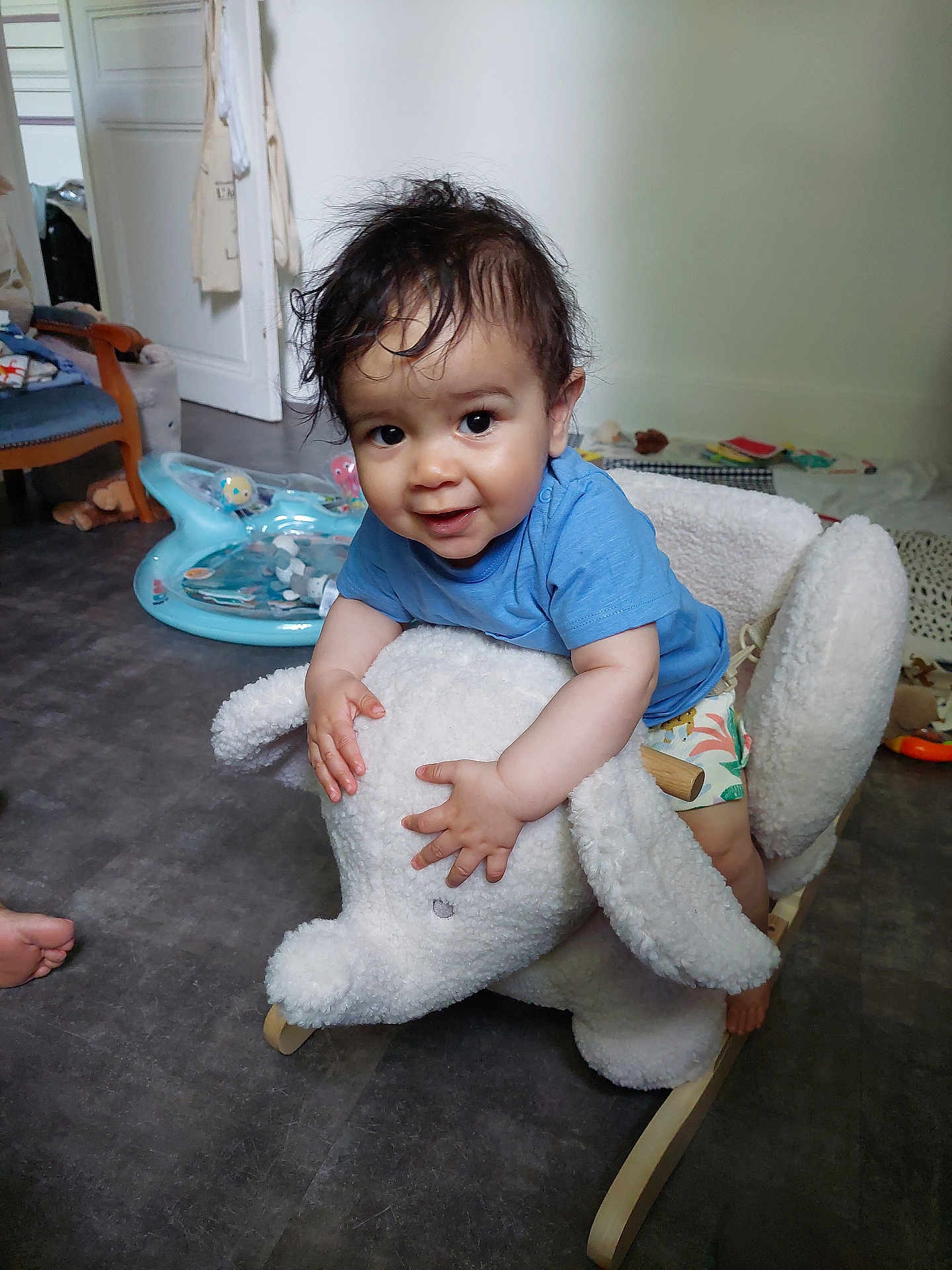 Maël a rejoint le concours — aidez-le/la à gagner de superbes lots ! blue_shirt, child, elephant, face, floor, foot, furniture, hair, hand, happy, home, indoor, person, play_area, plush, rocking_toy, shorts, smiling, toddler, toy