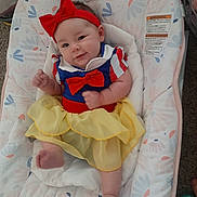 Muireann joined the competition — help win amazing prizes! baby, infant, child, smile, red_bow, yellow_skirt, blue_top, baby_seat, floral_pattern, indoor, cute, happy, portrait, headband, furniture, carpet, footwear_absent, skin, clothing, person