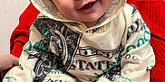Zachery is registered to the contest to win money with this photo: apparel, baby, casual, child, clothing, cozy, cute, expression, face, feet, happy, hoodie, indoors, infant, person, portrait, red_blanket, sitting, smile, young_child