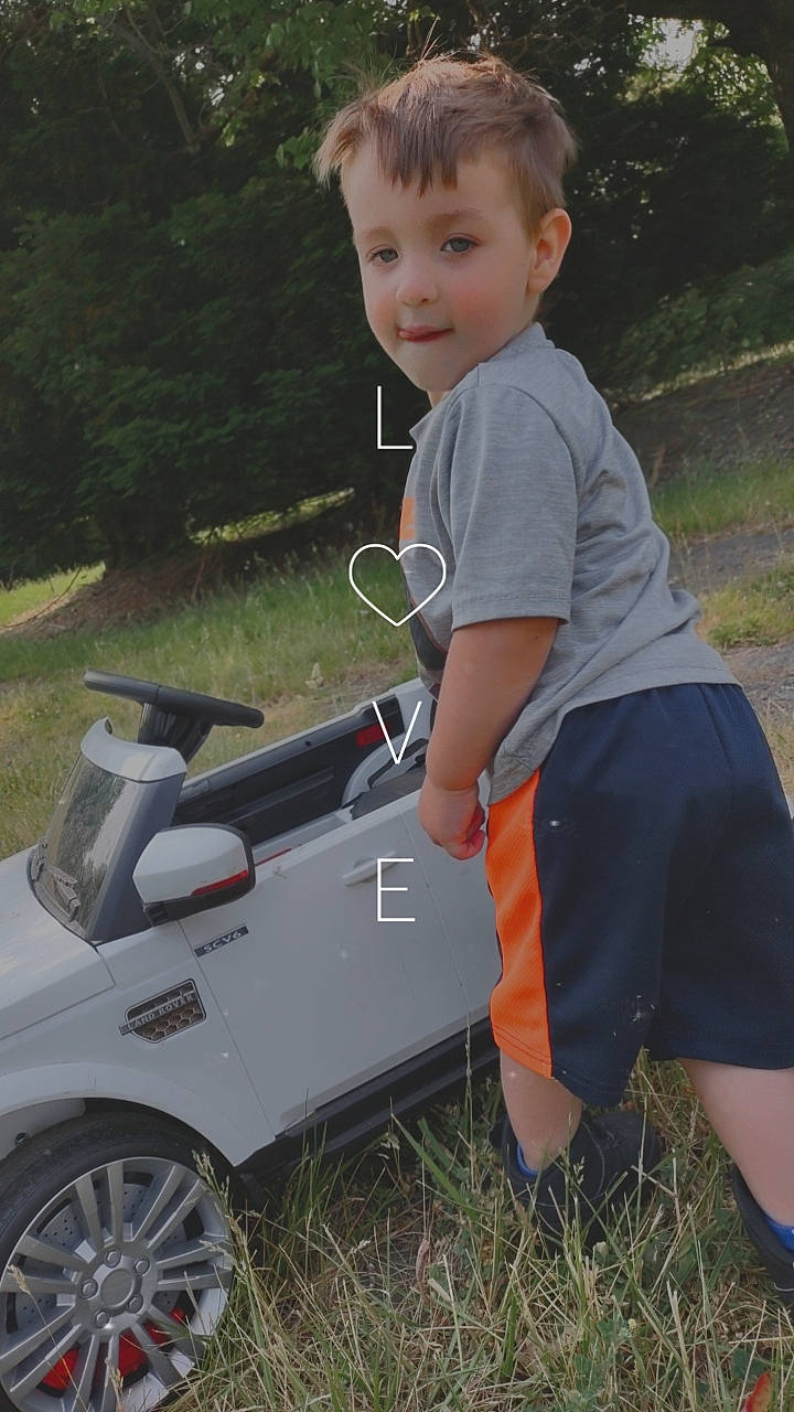 Ashton is registered to the contest to win money with this photo: automotive_design, automotive_exterior, automotive_tire, car, fender, grass, lawn, motor_vehicle, people_in_nature, person, plant, recreation, shorts, t_shirt, tire, toddler, toy, tree, vehicle, vehicle_door