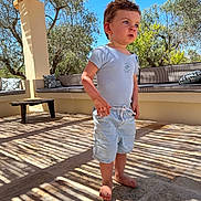 Paul a rejoint le concours — aidez-le/la à gagner de superbes lots ! toddler, child, barefoot, shorts, tshirt, outdoor, patio, shadows, wooden_pergola, pillows, bench, trees, sunlight, blue_sky, curious, standing, daylight, casual_clothing, nature, relaxing