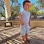 toddler, child, barefoot, shorts, tshirt, outdoor, patio, shadows, wooden_pergola, pillows, bench, trees, sunlight, blue_sky, curious, standing, daylight, casual_clothing, nature, relaxing