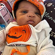 Kharia is registered to the contest to win money with this photo: baby, infant, child, face, clothing, hat, pumpkin, orange, white, cute, portrait, indoor, soft_lighting, closeup, expression, newborn, person, apparel, sitting, blanket