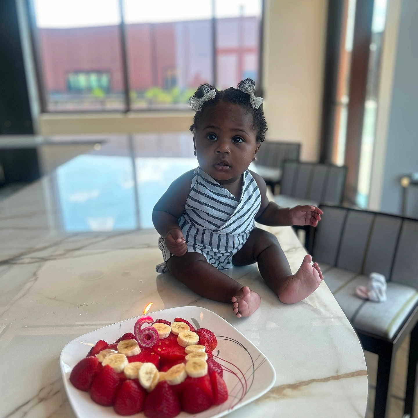 Tianna joined the competition — help win amazing prizes! baby, birthday_cake, candle, child, curly_hair, fruit, indoor, kitchen, marble_countertop, plate, person, sitting, strawberry, table, toddler, window, young_child, striped_clothing, celebration, food