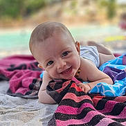 énola a rejoint le concours — aidez-le/la à gagner de superbes lots ! baby, smiling, towel, beach, sand, happy, child, outdoor, portrait, laying, cute, summer, colorful, striped, infant, playful, sunlight, nature, relaxing, barefoot