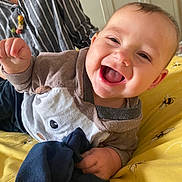Luke is registered to the contest to win money with this photo: baby, smiling, child, infant, bedspread, bee_pattern, plush_toy, clothing, person, striped_shirt, hand, face, happy, indoors, portrait, cute, young_child, fabric, closeup, joyful