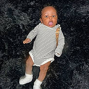 Terrance Iii is registered to the contest to win money with this photo: baby, infant, striped_onesie, white_socks, black_fur_rug, lying_down, surprised_expression, child, cute, soft_texture, indoors, small_person, human, adorable, newborn, face, head, limbs, clothing, portrait