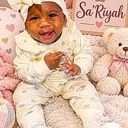 Sariyah is registered to the contest to win money with this photo: baby, child, infant, smiling, portrait, sitting, bow_headband, curly_hair, onesie, sneakers, teddy_bear, stuffed_animal, blanket, plush, pastel, hearts, nursery, name_sign, indoor, studio_photography