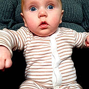 Tommie joined the competition — help win amazing prizes! adult, baby, blue_eyes, buttoned_clothing, child, close_up, cozy, curious, expression, hand, indoor, knitted, pajamas, person, portrait, seated, soft_lighting, striped_clothing, sweater, texture