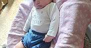 Irie is registered to the contest to win money with this photo: baby, infant, child, reclining, pink_blanket, blue_shorts, white_shirt, indoor, carpet, cushion, soft_fabric, young_child, floor, curious_expression, comfortable, casual_clothing, home, person, portrait, relaxed