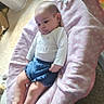 baby, infant, child, reclining, pink_blanket, blue_shorts, white_shirt, indoor, carpet, cushion, soft_fabric, young_child, floor, curious_expression, comfortable, casual_clothing, home, person, portrait, relaxed