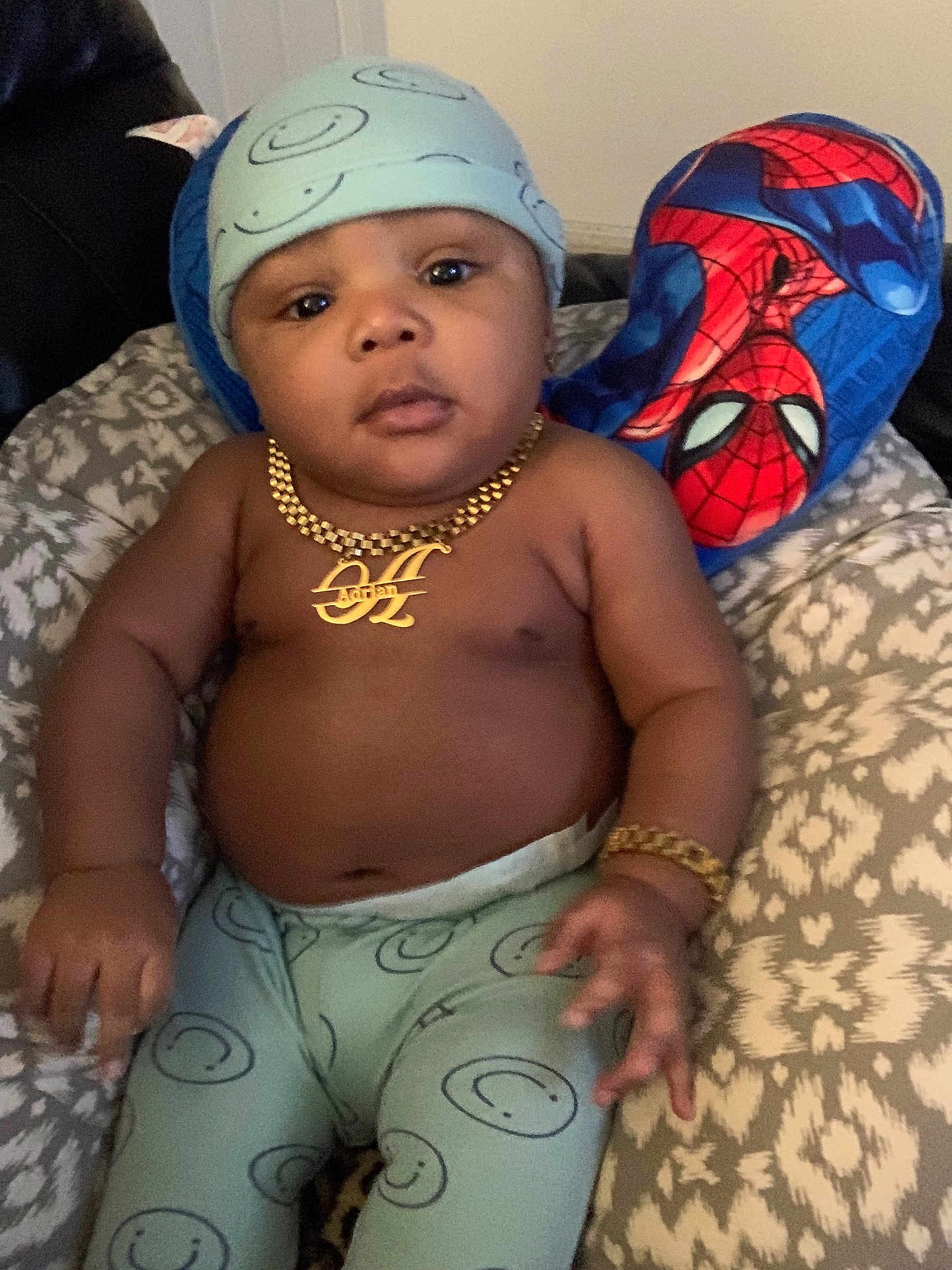 Adrian joined the competition — help win amazing prizes! baby, child, smiling_face, hat, pants, gold_necklace, gold_bracelet, spiderman_pillow, cushion, patterned_fabric, indoor, person, portrait, baby_clothing, accessory, relaxing, furniture, cute, young_child, seated