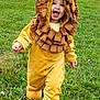 child, toddler, lion_costume, yellow, brown, grass, outdoor, smiling, happy, cute, walking, costume, nature, greenery, playful, baby, face, hood, fun, joy