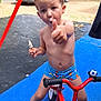 child, toddler, ice_cream, thumbs_up, tricycle, swim_shorts, bare_chest, blue_mat, summer, outdoor, campground, cars, trees, laundry, playful, sticky, bare_feet, portrait, vehicle, toy_ball