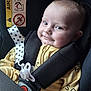 baby, car_seat, child, infant, seatbelt, pacifier, yellow_clothing, polka_dots, star_pattern, smile, face, head, straps, safety, indoor, warning_sign, closeup, cute, expression, seat