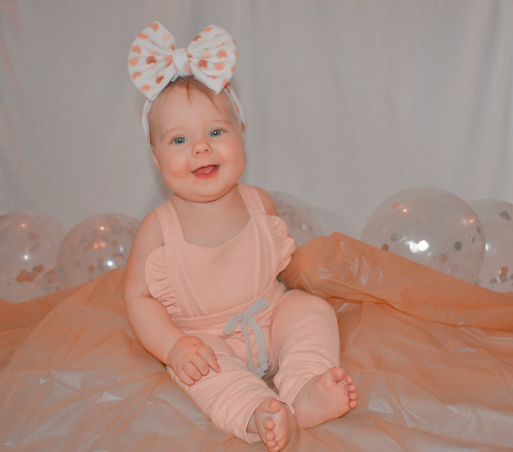 Oakley is registered to the contest to win money with this photo: arm, baby, baby_toddler_clothing, comfort, dress, event, eye, fun, happy, head, headband, headpiece, human_leg, jewellery, joy, peach, person, pink, skin, sleeve