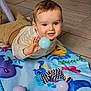 baby, child, play_mat, toy_ball, floor_tiles, indoor, happy, smiling, clothing, striped_shirt, pants, hand, face, head, blue_eyes, cute, teething_toy, colorful, playtime, lying_down