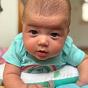 Arlee is registered to the contest to win money with this photo: baby, infant, child, face, eyes, skin, tshirt, rainbow, arm, hand, pillow, soft_toys, indoors, closeup, portrait, cute, expression, lying_down, person, young