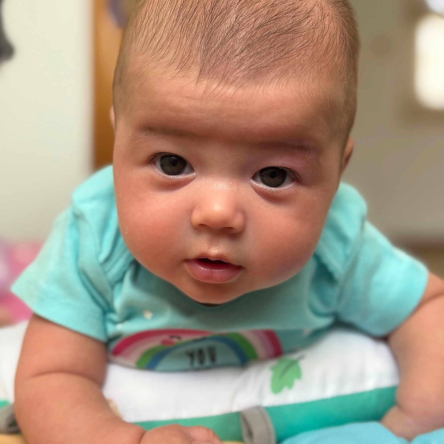 Arlee is registered to the contest to win money with this photo: arm, baby, child, closeup, cute, expression, eyes, face, hand, indoors, infant, lying_down, person, pillow, portrait, rainbow, skin, soft_toys, tshirt, young