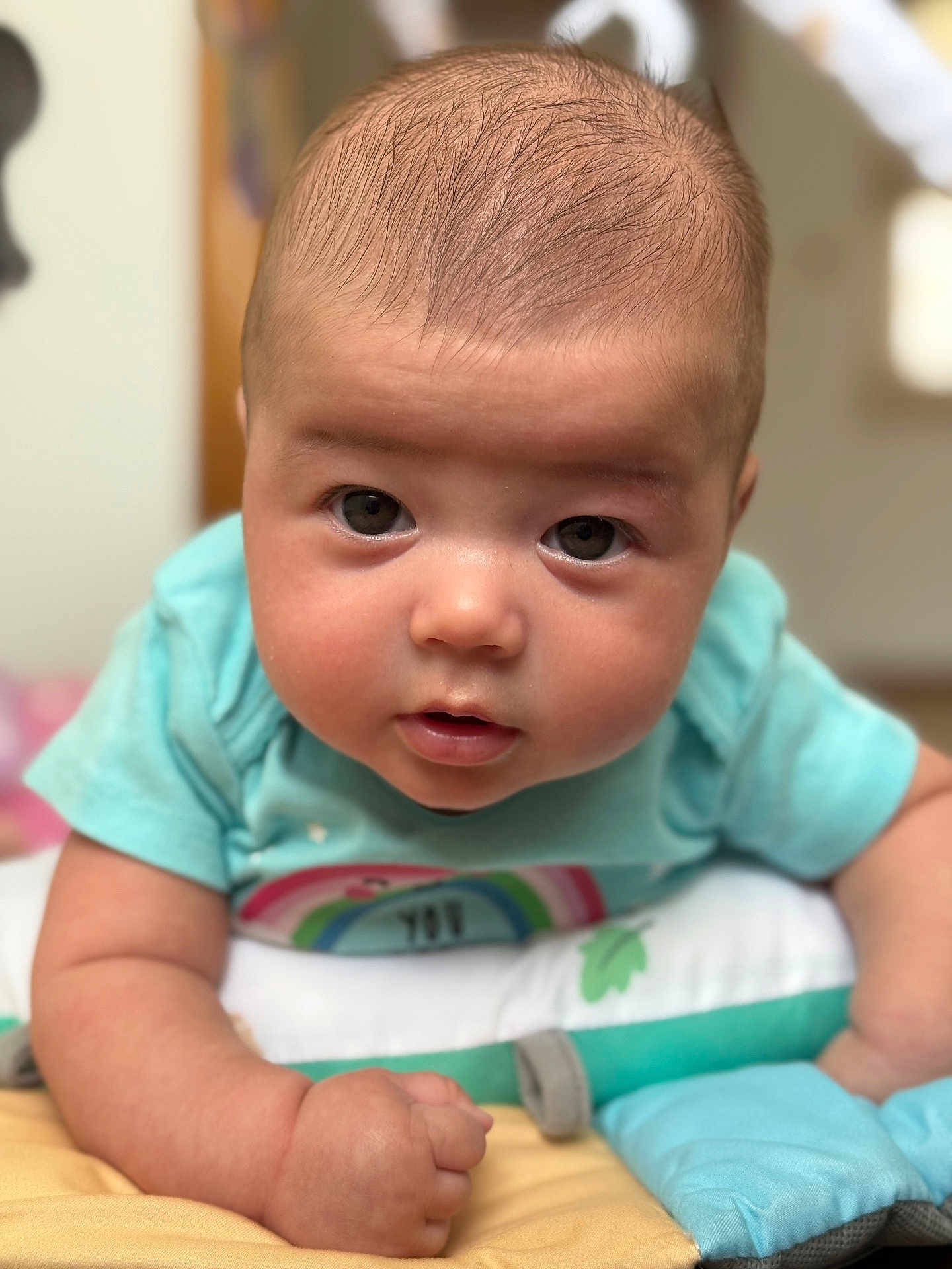 Arlee is registered to the contest to win money with this photo: baby, infant, child, face, eyes, skin, tshirt, rainbow, arm, hand, pillow, soft_toys, indoors, closeup, portrait, cute, expression, lying_down, person, young