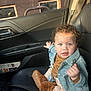 child, toddler, curly_hair, blue_eyes, denim_jacket, holding_keys, car_interior, passenger_seat, leather_seat, seatbelt, boots, baby_clothes, sitting, portrait, sunlight, window, door_panel, magazine, hand, expression