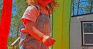 Nova is registered to the contest to win money with this photo: blonde_hair, blue_sky, boots, building, child, colorful, daytime, fun, grass, happy, inflatable_bounce_house, outdoor, overalls, play, shadow, smile, sunlight, toddler, trees, window