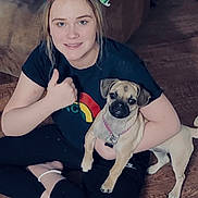 Lucy is registered to the contest to win money with this photo: black_shirt, casual_clothing, collar, couch, cute, dog, festive_headband, floor, girl, happy, home, indoor, light_brown_dog, pet, sitting, small_dog, smiling, thumbs_up, wooden_floor, young_person