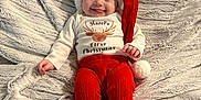 Hazel joined the competition — help win amazing prizes! baby, infant, smiling, tongue_out, santa_hat, red_pants, onesie, christmas, holiday, blanket, soft_texture, cute, lying_down, happy, festive, child, portrait, indoor, cozy, celebration