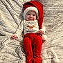 baby, infant, smiling, tongue_out, santa_hat, red_pants, onesie, christmas, holiday, blanket, soft_texture, cute, lying_down, happy, festive, child, portrait, indoor, cozy, celebration