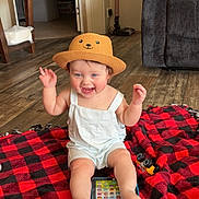 Weston joined the competition — help win amazing prizes! baby, child, hat, toy, blanket, indoor, floor, smiling, sitting, rattle, cube, tablet_toy, furniture, couch, wood_floor, clothing, happy, toy_car, living_room, person