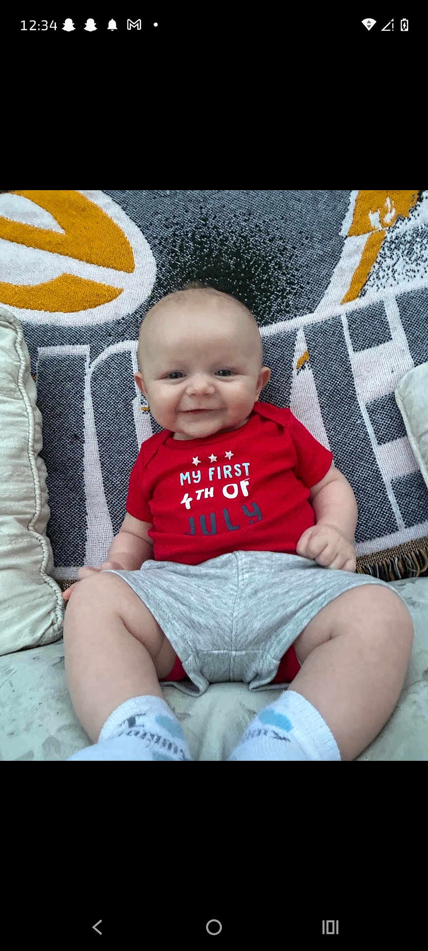Easton joined the competition — help win amazing prizes! baby, infant, smiling, red_shirt, sitting, pillow, blanket, cute, happy, indoor, child, young, celebration, holiday, footwear, sock, clothing, face, portrait, couch