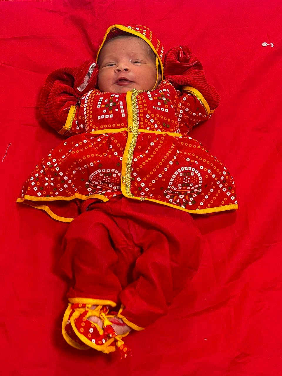 Reyna joined the competition — help win amazing prizes! baby, infant, red_clothing, traditional_outfit, lying_down, colorful, cute, child, face, headwear, footwear, patterned_clothing, fabric, soft, small_hands, portrait, indoors, celebration, bright_colors, warm