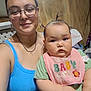 Scarlette joined the competition — help win amazing prizes! woman, baby, indoor, glasses, bib, tank_top, person, child, portrait, smile, serious, hair, pigtails, earrings, necklace, wooden_wall, window, home, casual, holding