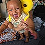 baby, smiling, child, person, indoor, plush_toy, yellow, living_room, couch, adult, holding, happy, clothing, infant, hand, face, furniture, home, cheerful, playful