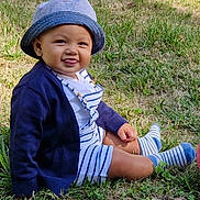 Colin participe au concours pour gagner de l'argent avec cette photo : baby, child, grass, hat, striped_clothing, cardigan, socks, tongue_out, outdoor, cute, smiling, sitting, nature, sunlight, happy, person, infant, casual_wear, summer, playful