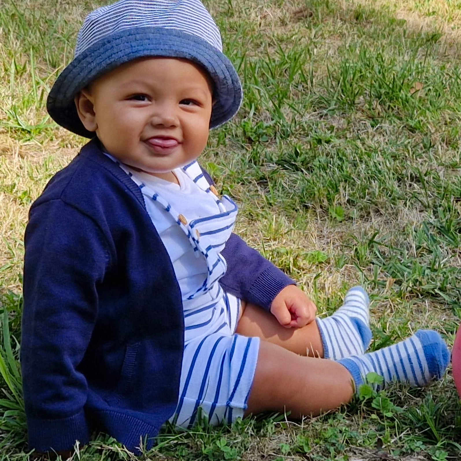 Colin participe au concours pour gagner de l'argent avec cette photo : baby, cardigan, casual_wear, child, cute, grass, happy, hat, infant, nature, outdoor, person, playful, sitting, smiling, socks, striped_clothing, summer, sunlight, tongue_out